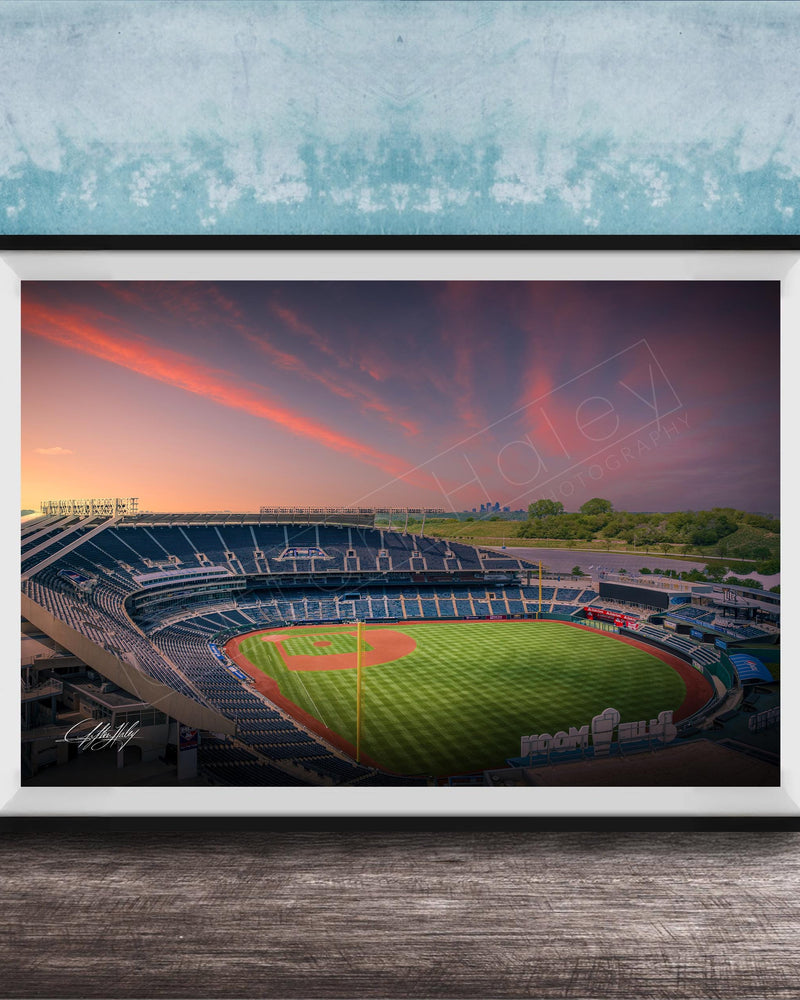 A framed photograph of a baseball stadium at sunset, with the field illuminated by the warm glow of the setting sun.