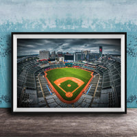 A framed photograph of a baseball stadium with a large field, surrounded by buildings and a cloudy sky.