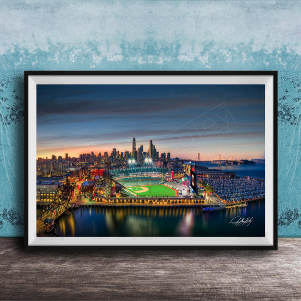 A framed aerial view of a city skyline at night, with a brightly lit stadium and surrounding buildings.