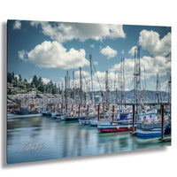 A row of sailboats docked in a harbor, with a backdrop of mountains and a partly cloudy sky.