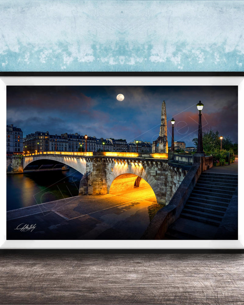 a picturesque night scene of a bridge illuminated by warm lighting, with a full moon in the sky and a tall spire in the background.
