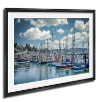 A framed photograph depicting a harbor filled with numerous sailboats docked in the water, with a cloudy blue sky overhead.
