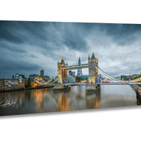a cityscape with a large suspension bridge spanning a river, with the bridge's towers illuminated against a cloudy sky.