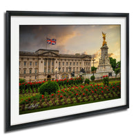 A framed photograph of Buckingham Palace in London, England, with the Union Jack flag flying in the background and a statue of a golden angel on a pedestal.