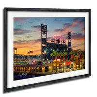 A framed photograph depicting a baseball stadium at sunset, with the stadium lights and surrounding palm trees illuminated against a colorful sky.