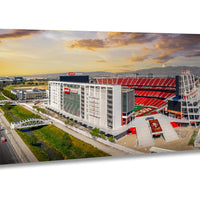 a large stadium with a red roof and white walls, surrounded by a large parking lot and a bridge. The stadium appears to be a sports venue, possibly a professional sports stadium.