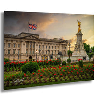A large, ornate building with a flag flying above it, surrounded by a well-maintained garden with red flowers.