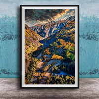 The image is a framed photograph of a winding mountain road surrounded by lush forests and autumnal trees, with a dramatic sky in the background.