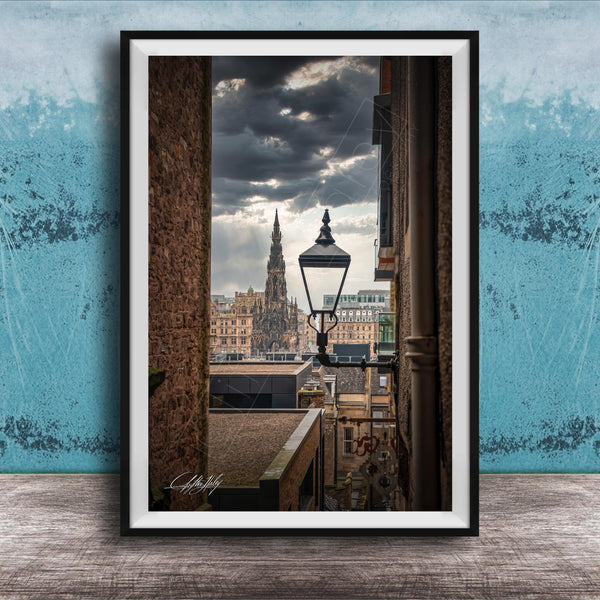 a cityscape with a tall, ornate building in the background, framed in a black frame and placed on a wooden surface against a blue wall.