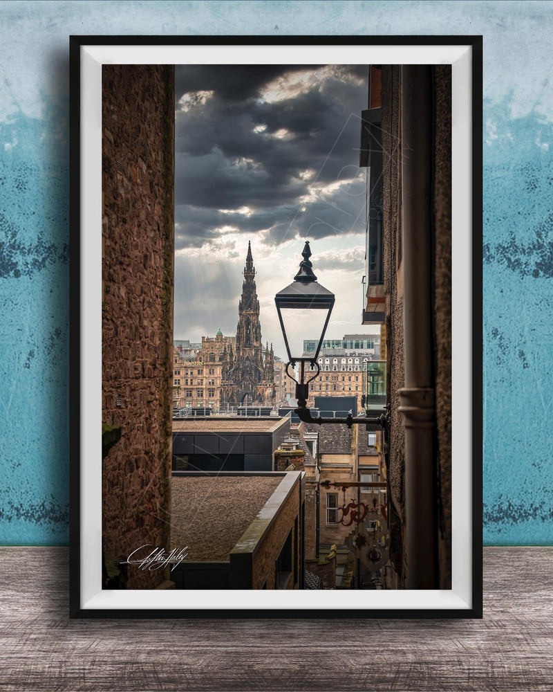a cityscape with a tall, ornate building in the background, framed in a black frame and placed on a wooden surface against a blue wall.
