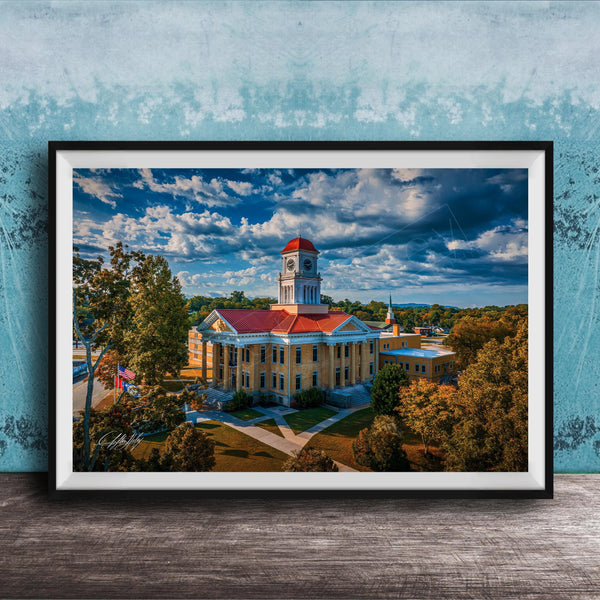 A framed photograph of a large, ornate building with a red roof and a clock tower, surrounded by trees and a blue sky with clouds.