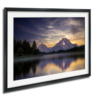 a serene landscape with a mountain range reflected in a calm lake, surrounded by lush greenery and a dramatic sky with clouds.