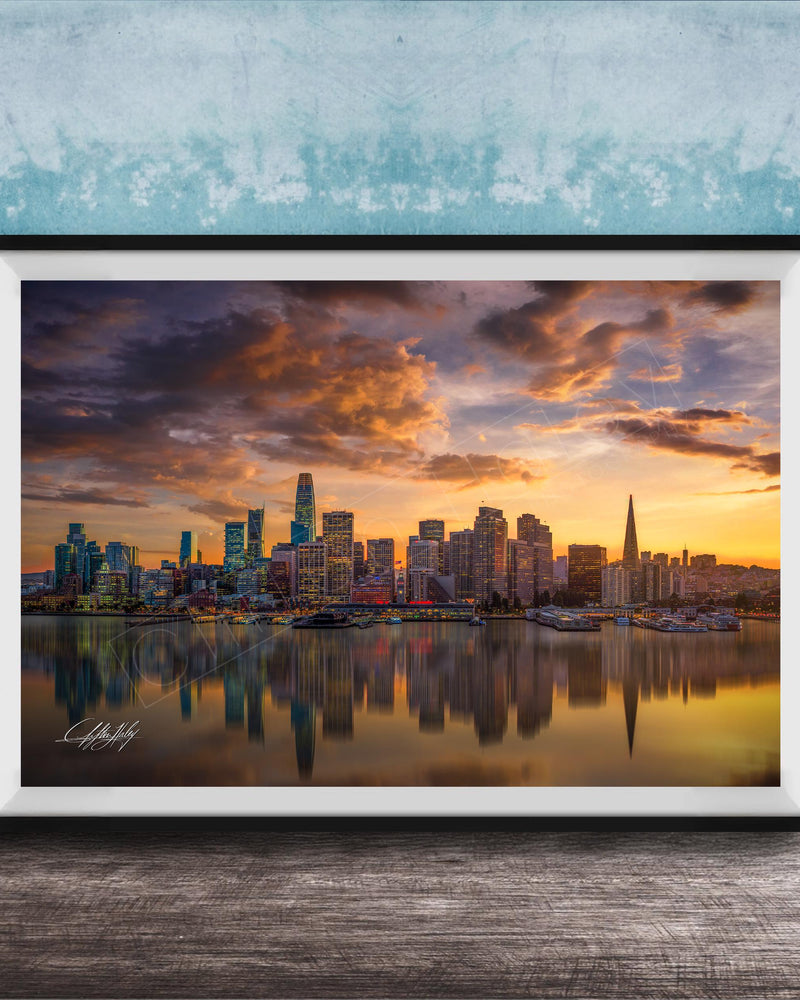 A framed photograph depicting a city skyline at sunset, with the city's buildings reflected in the water below.