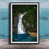 A framed photograph of a waterfall cascading down a rocky cliff surrounded by lush greenery, with a blue-green body of water below.