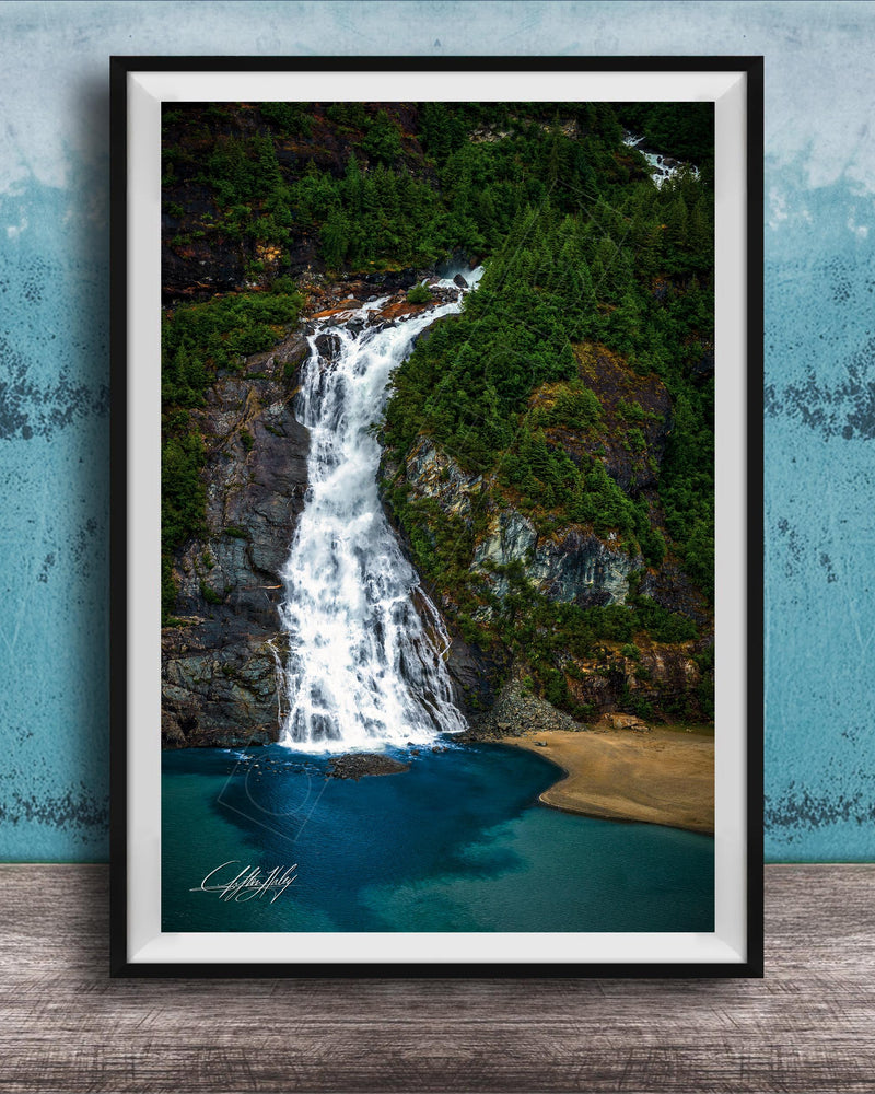 A framed photograph of a waterfall cascading down a rocky cliff surrounded by lush greenery, with a blue-green body of water below.