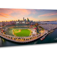 An aerial view of a baseball stadium with a city skyline in the background, set against a colorful sunset sky.