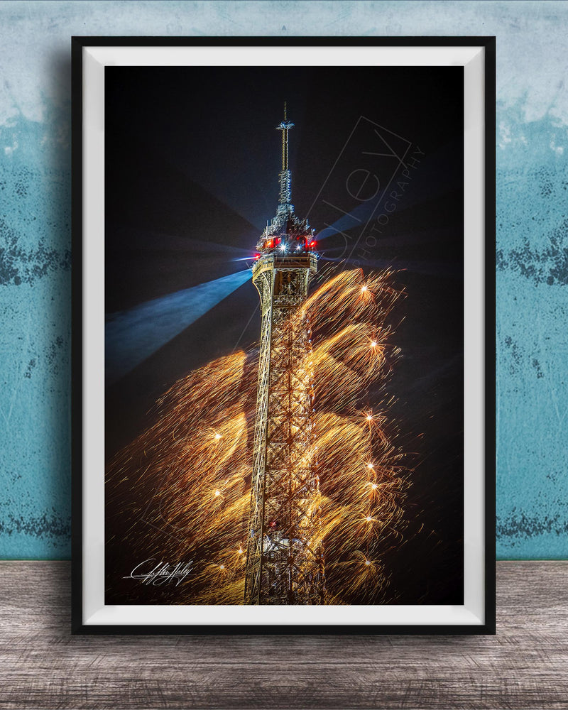 A framed photograph of the Eiffel Tower with a fireworks display in the background, creating a vibrant and colorful scene.