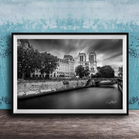 A black and white photograph of the Notre-Dame Cathedral in Paris, France, with a river and trees in the foreground.