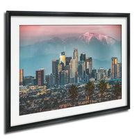 A framed photograph of the Los Angeles skyline at sunset, with the city's skyscrapers and mountains in the background.