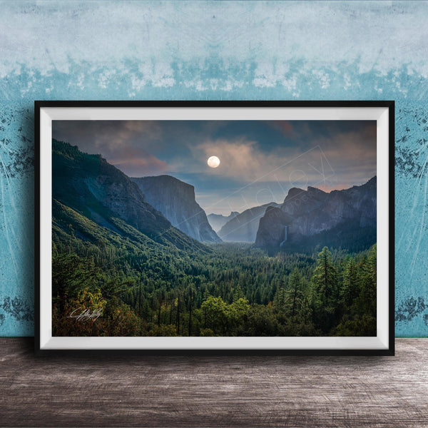 The image is a framed photograph of a mountainous landscape with a full moon in the sky, surrounded by trees and forests.