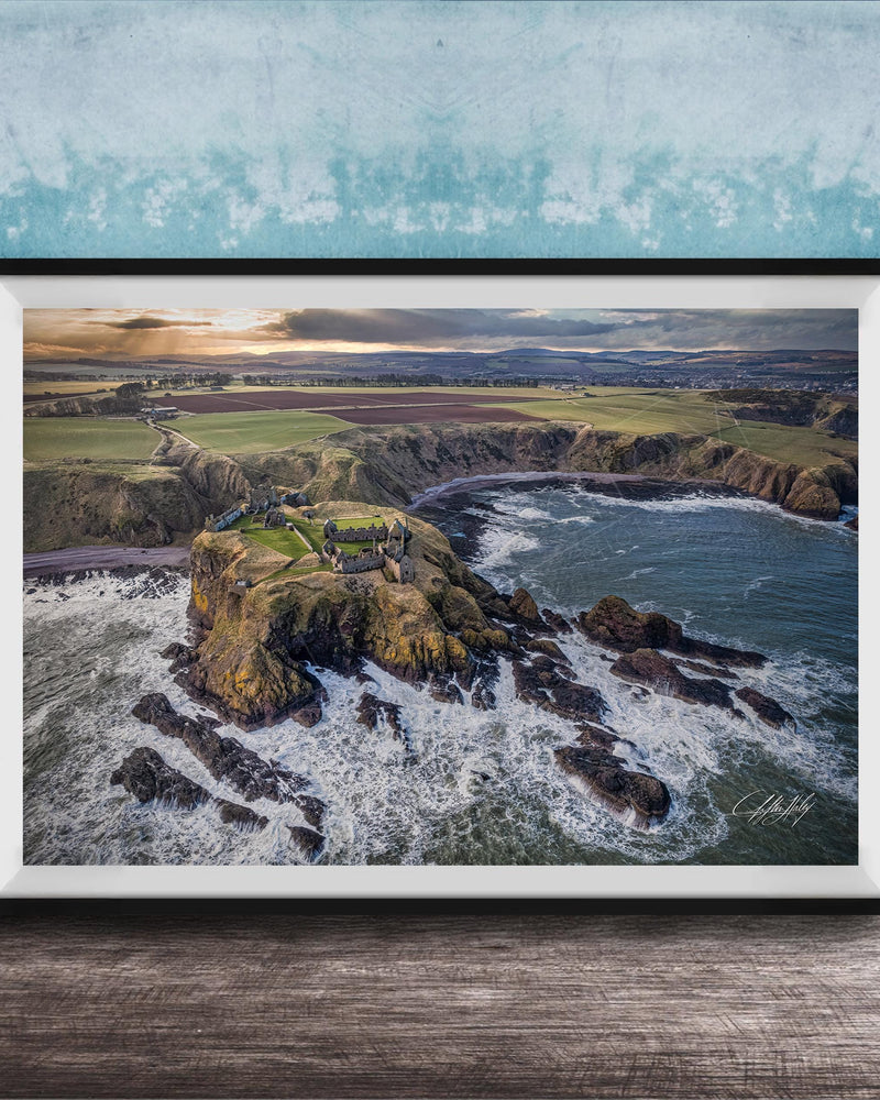 The image is a framed aerial view of a coastal landscape, featuring a rocky outcrop, a small island, and the ocean.