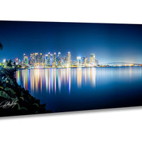 A stunning nighttime cityscape with a skyline of illuminated buildings reflected in the calm waters of a large body of water, creating a mesmerizing and vibrant scene.