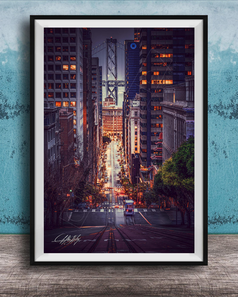 A framed photograph depicting a city street at night, with tall buildings and a bridge in the background. The street is illuminated by streetlights and the glow of the buildings, creating a vibrant and dynamic scene.