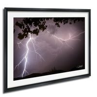 A framed photograph depicting a dramatic lightning storm with bolts of light illuminating the dark sky.