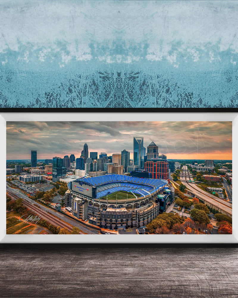 The image is a framed aerial view of a city skyline, featuring a large stadium with a distinctive blue roof.