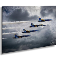 four blue US Navy fighter jets flying in a tight formation through a cloudy sky.