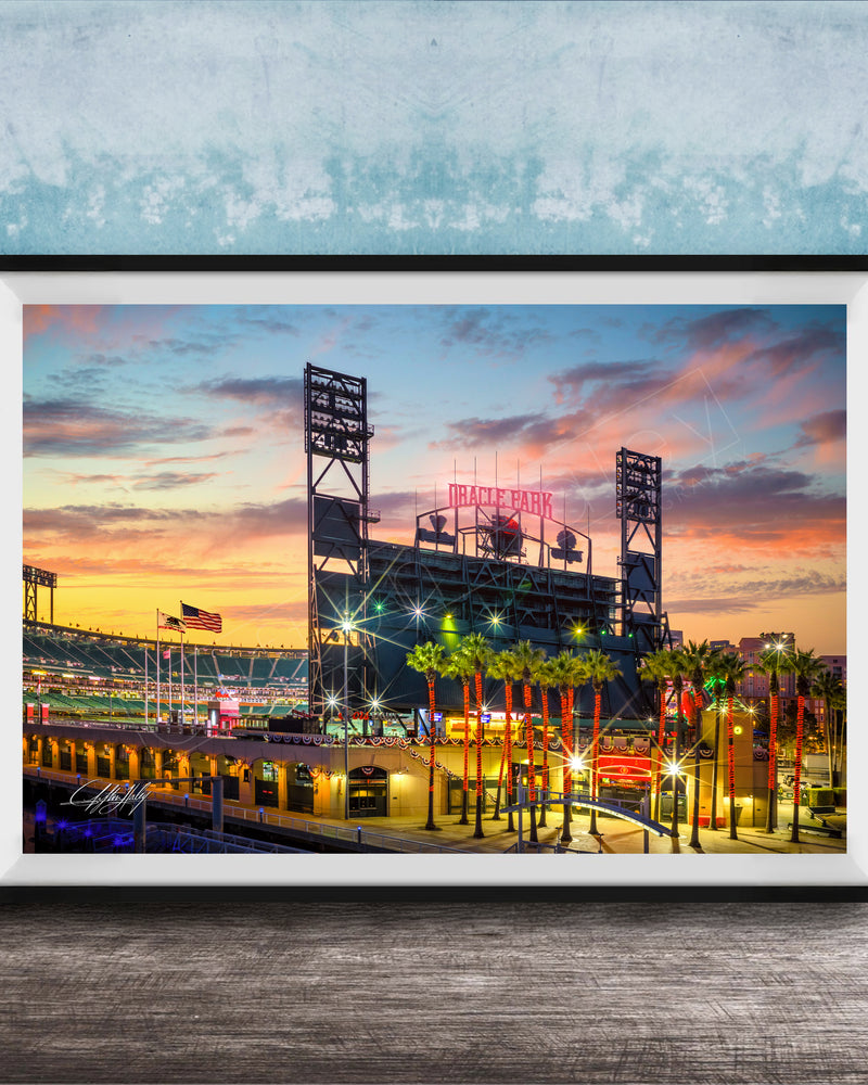 A framed photograph of a baseball stadium at sunset, with the stadium's lights and surrounding palm trees illuminated against a colorful sky.