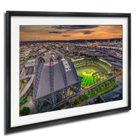 The image is an aerial view of a baseball stadium with a large field and surrounding cityscape at sunset.