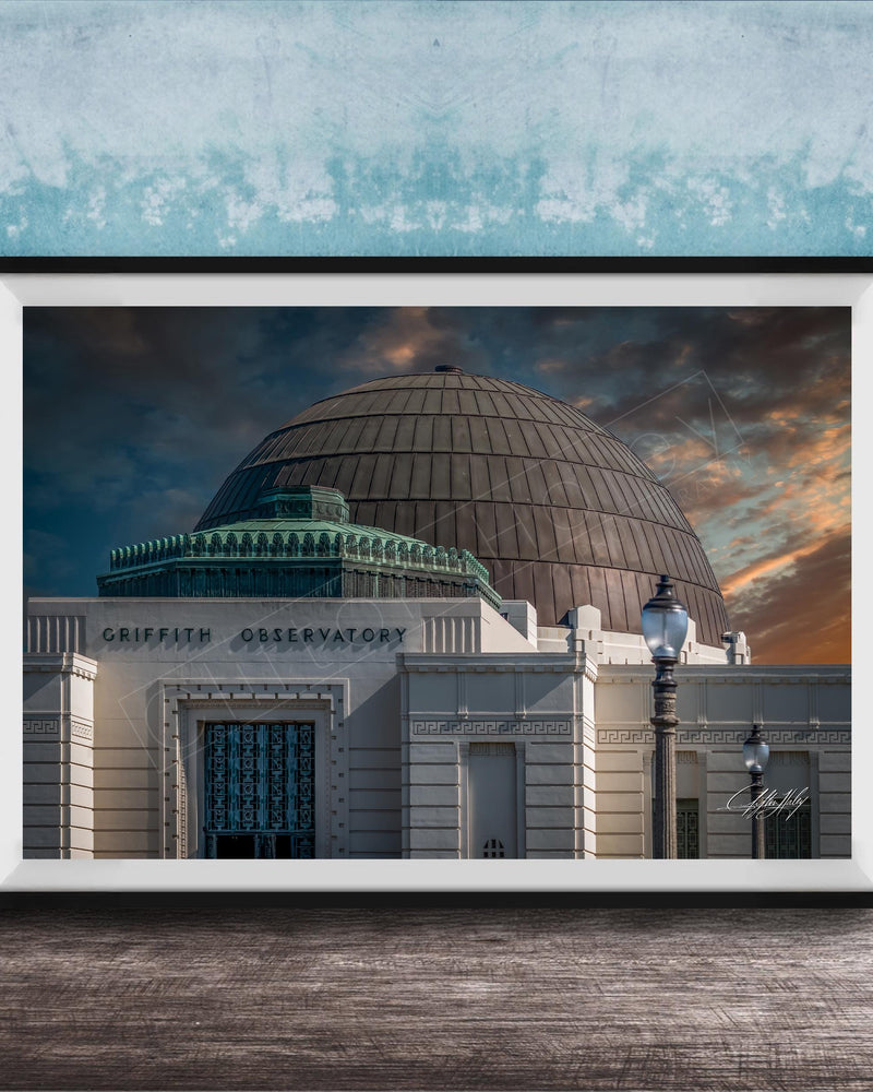 the Griffith Observatory, a large domed building with a distinctive architectural style, set against a dramatic sky with clouds and a sunset.