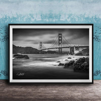 A black and white photograph of the Golden Gate Bridge in San Francisco, California, with the bridge's towers and suspension cables prominently featured against a cloudy sky.