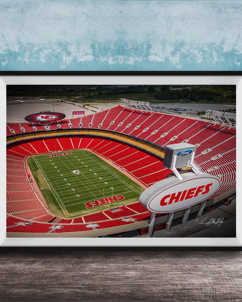 The image is a framed photograph of a football stadium, specifically the Kansas City Chiefs stadium, with the team's logo prominently displayed on the field.