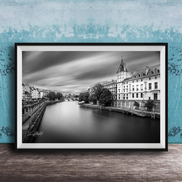 A black and white photograph of a cityscape with a river running through it, featuring a tall building with a clock tower in the background.