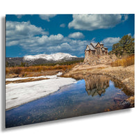 A picturesque scene of a stone house perched on a rocky outcrop, overlooking a serene lake and snow-capped mountains in the distance.
