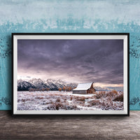 A framed photograph depicting a snowy mountain landscape with a wooden barn in the foreground, set against a cloudy sky.