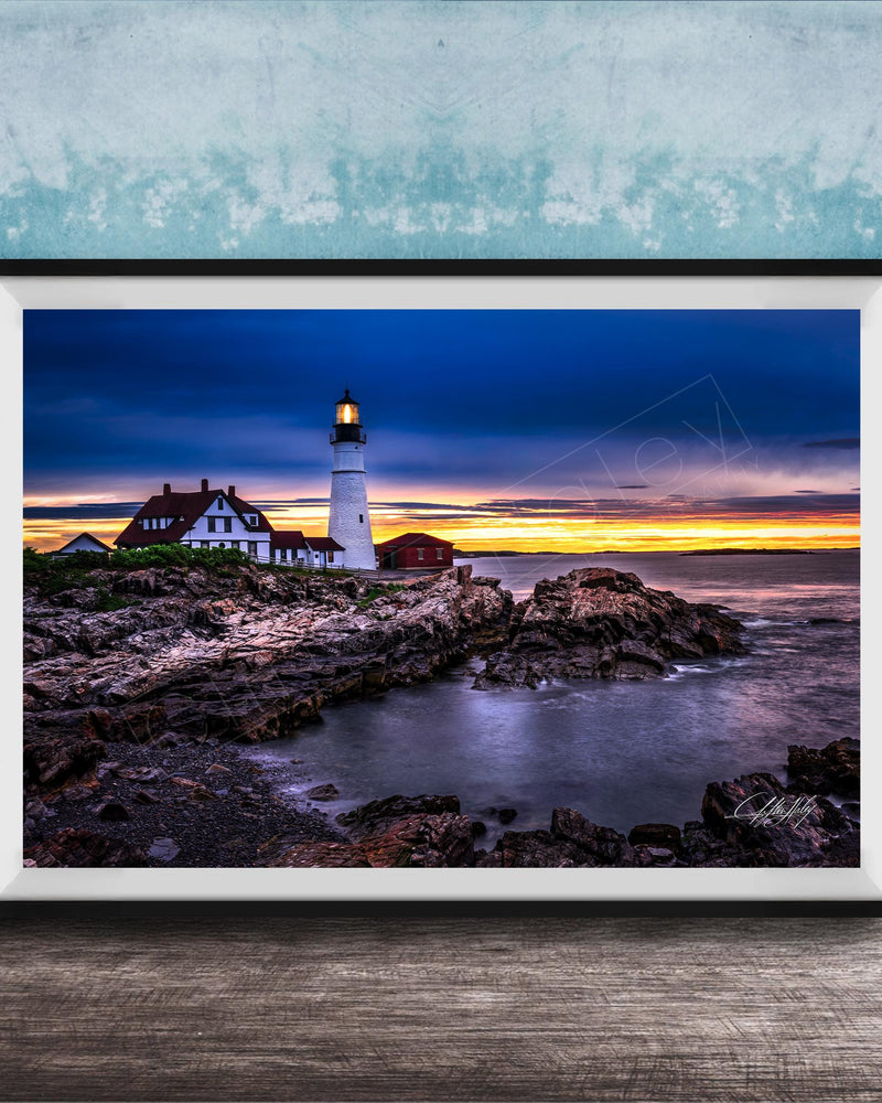 A framed photograph depicting a lighthouse on a rocky shore at sunset, with the sky filled with vibrant colors and the ocean reflecting the warm hues.