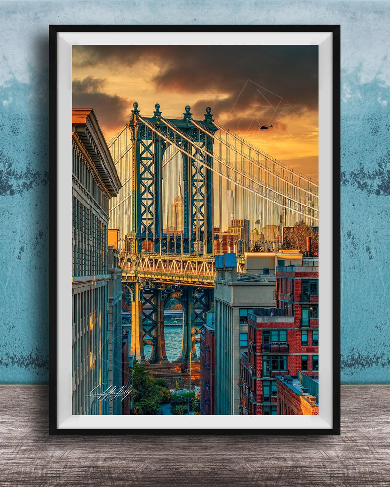 The image is a framed photograph of the Manhattan Bridge in New York City, with the bridge and surrounding buildings illuminated by a colorful sunset sky.
