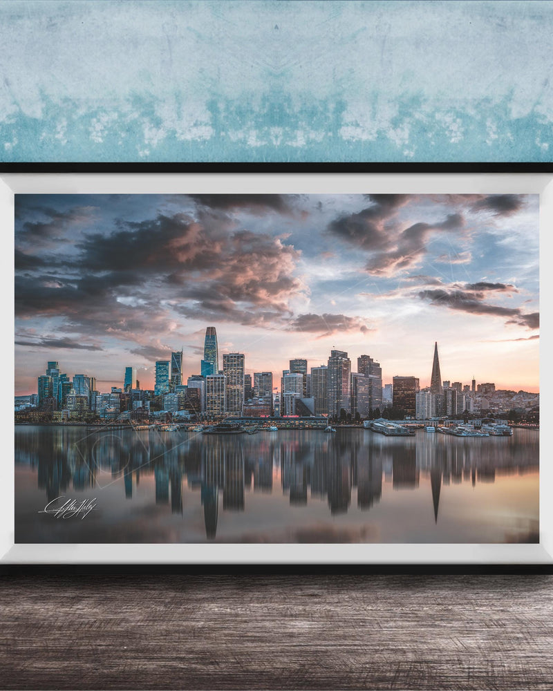 A framed photograph of a city skyline at sunset, with the buildings reflected in the water below.
