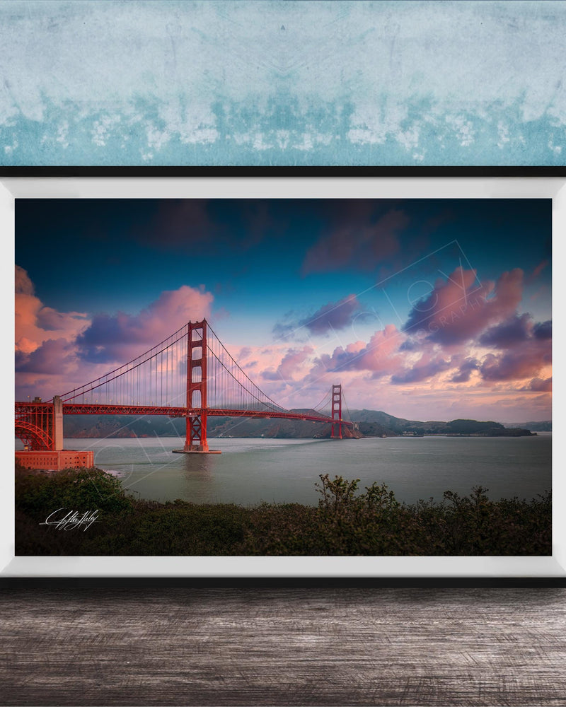 A framed photograph of the Golden Gate Bridge at sunset, with the bridge's distinctive red towers and suspension cables silhouetted against a colorful sky.