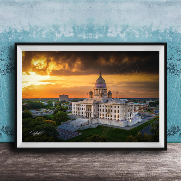 A framed photograph of a large, ornate building with a domed roof, set against a dramatic sky with orange and yellow hues, likely at sunset.