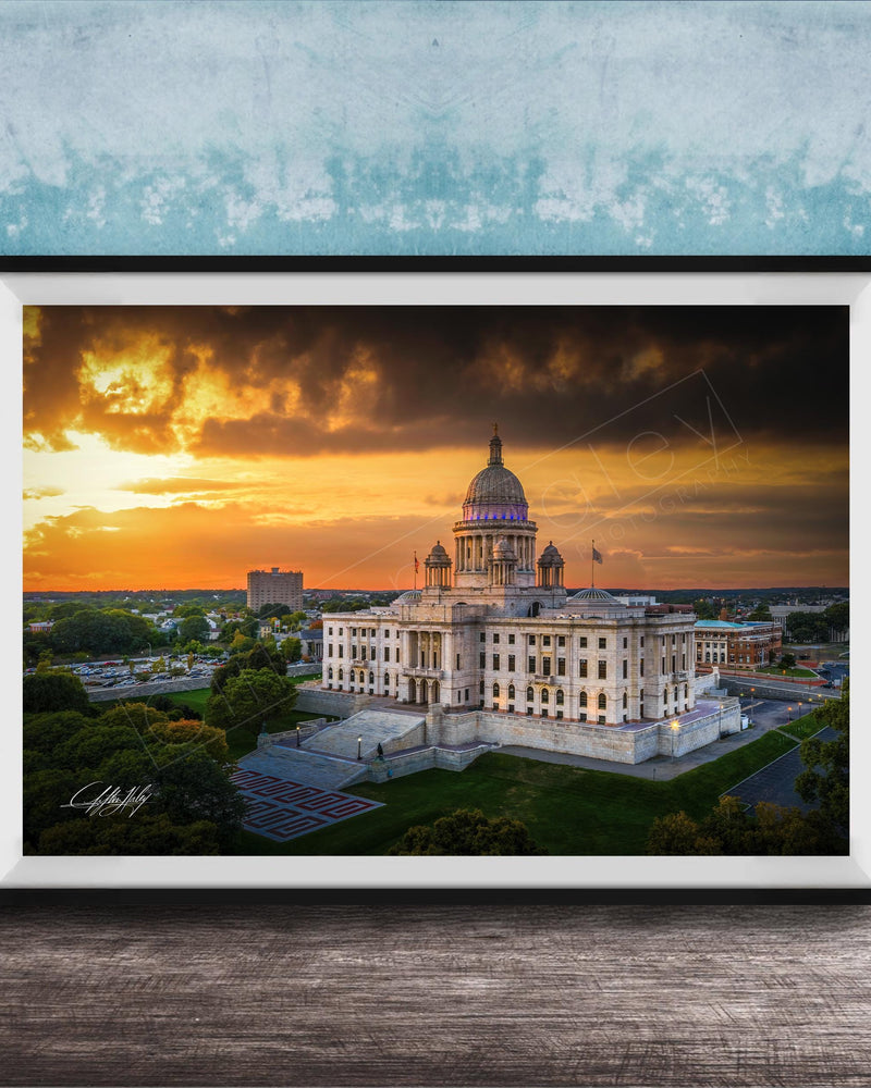 A framed photograph of a large, ornate building with a domed roof, set against a dramatic sky with orange and yellow hues, likely at sunset.