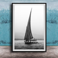 This luxury black and white fine art photograph captures a felucca sail boat drifting along the Nile River at sunset near Luxor, Egypt. Soft fog and minimalist composition create a timeless, monochrome aesthetic rooted in Egyptian river culture. Ideal for collectors and interior designers seeking refined, museum-quality wall art that embodies elegance, simplicity, and enduring calm.