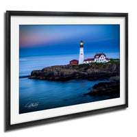 A framed photograph depicting a lighthouse on a rocky coastline, with the ocean in the background.