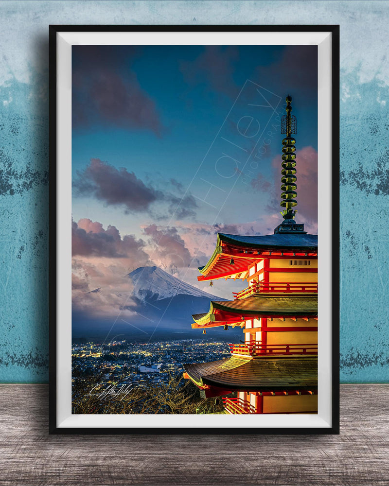 A framed photograph of a traditional Japanese pagoda, with a mountain range visible in the background, set against a blue sky with clouds.
