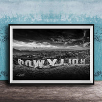 A black and white photograph of the Hollywood Sign, a famous landmark in Los Angeles, California. The sign is prominently displayed in the foreground, with the city skyline visible in the background.