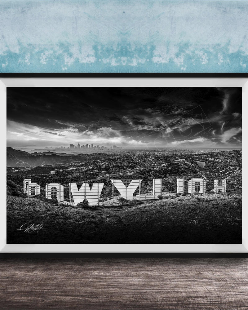 A black and white photograph of the Hollywood Sign, a famous landmark in Los Angeles, California. The sign is prominently displayed in the foreground, with the city skyline visible in the background.