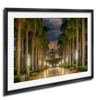 a serene and picturesque scene of a palm-lined pathway leading towards a mosque at night, with the mosque's dome and spire illuminated against a dark sky.